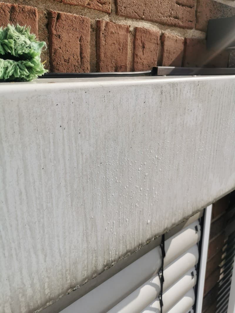 Nahaufnahme einer verschmutzten Fassade eines Gebäudes, die gereinigt wird. Im Hintergrund sind Ziegelsteine und Jalousien sichtbar.